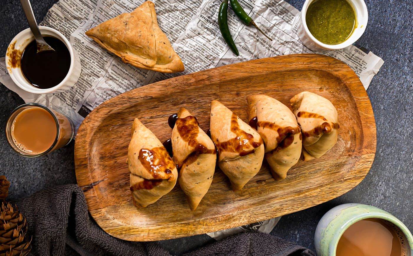 A tray of samosas with chutneys and cups of chai
