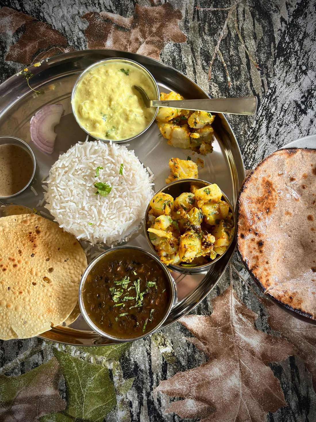 A steel thali with dal, rice, potato sabzi, papad and rotis